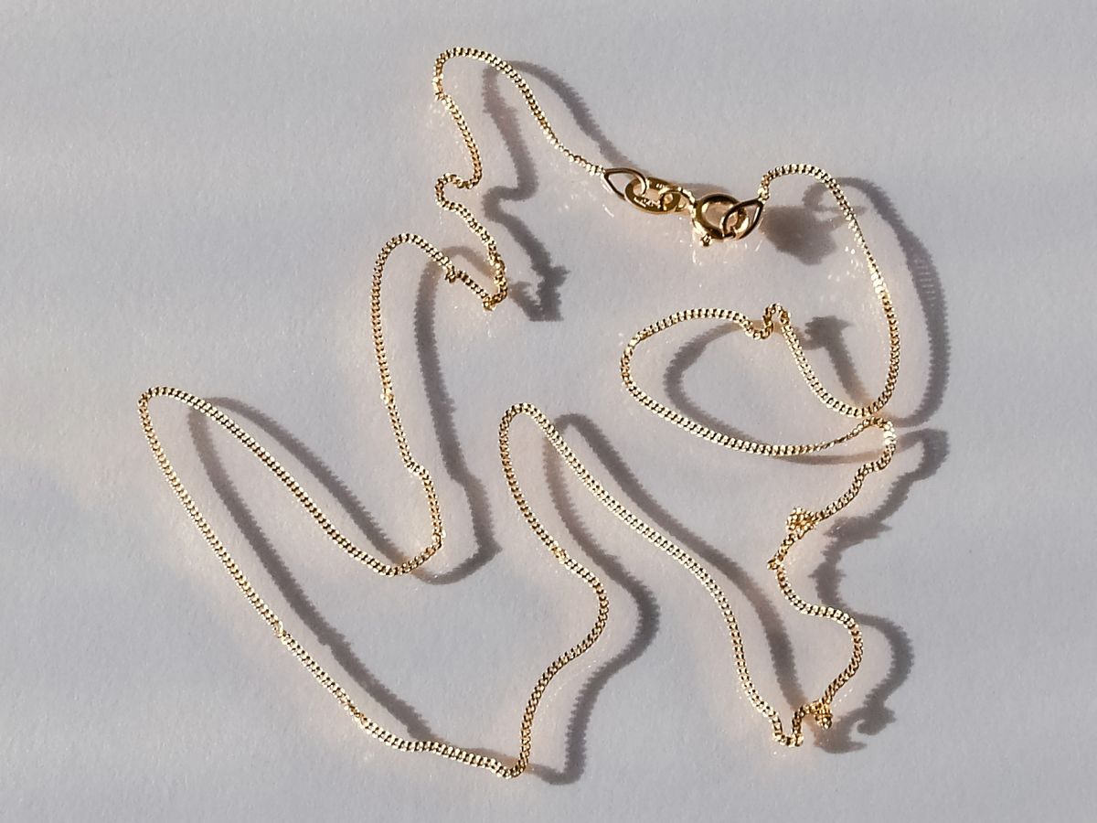 Thin 18k gold curb chain with clasp, laid loosely on a white surface