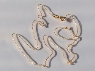 Thin 18k gold curb chain with clasp, laid loosely on a white surface
