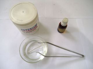 Jewelry testing acids on a bench: a jar, a small bottle and a glass dish with tweezers