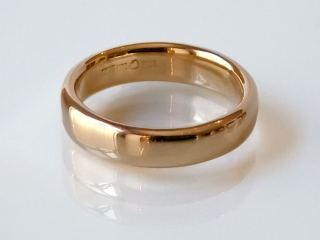Plain polished 18k gold band on a white surface, hallmarks visible on the inside