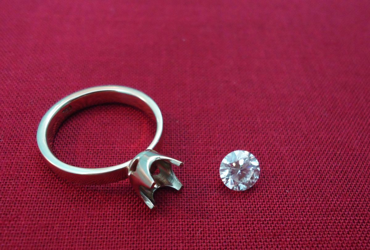 Empty solitaire ring setting with its round brilliant stone lying beside it on red cloth